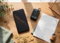 A wooden desk with a phone and a hardware wallet and gold coins in warm copper light, showing the Binance hack and why custody matters.