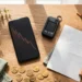 A wooden desk with a phone and a hardware wallet and gold coins in warm copper light, showing the Binance hack and why custody matters.